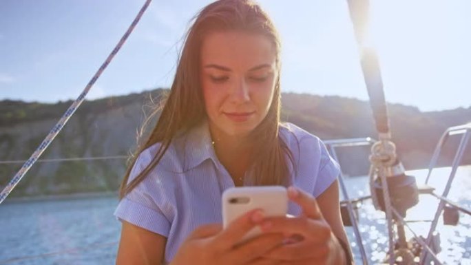 SLO MO LD年轻女子在阳光下的游艇上在智能手机上打字
