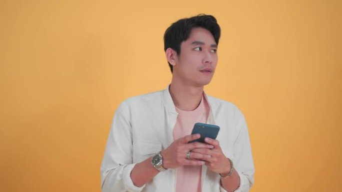 年轻的亚洲男子使用移动智能手机在孤立的工作室黄色背景工作室肖像。面部表情，惊讶于激动人心的微笑和快乐