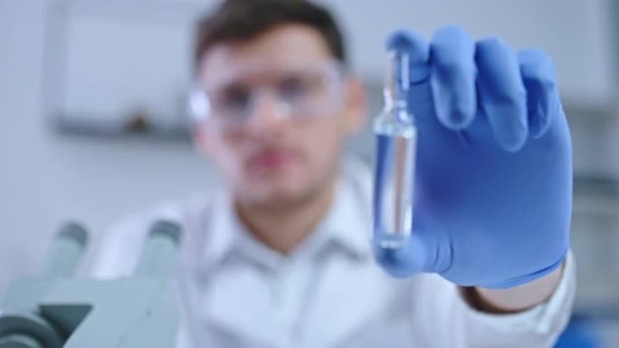 严肃的男性科学家在cam上显示安瓿与药物，实验室研究