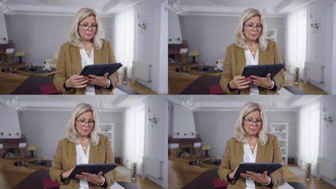 站在室内的平板电脑上，沉迷于眼镜中的女人上网。严肃的高加索专家心理学家在办公室在线阅读最新新闻的肖像