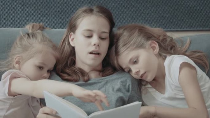 家庭阅读时间。三个小姐妹在沙发上看书，互相拥抱