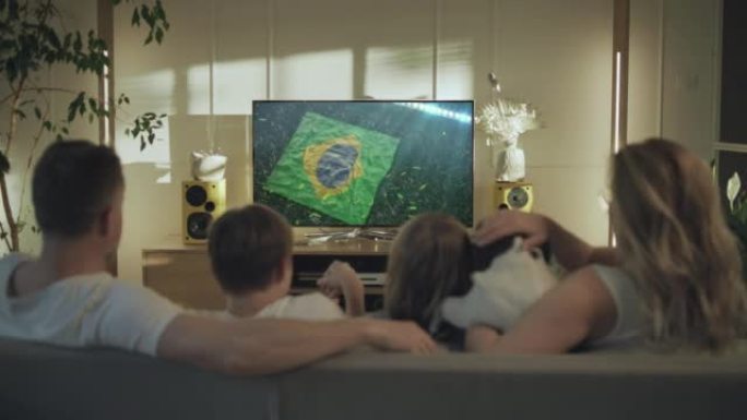母亲父亲和两个孩子带着狗看电视。摄像机在屏幕上迅速向巴西国旗移动
