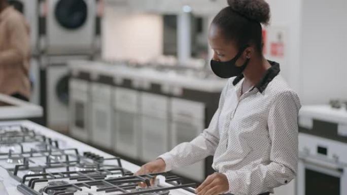 游客在购物中心的家电商店购物，年轻的非洲裔美国妇女正在看煤气炉，为厨房选择新设备