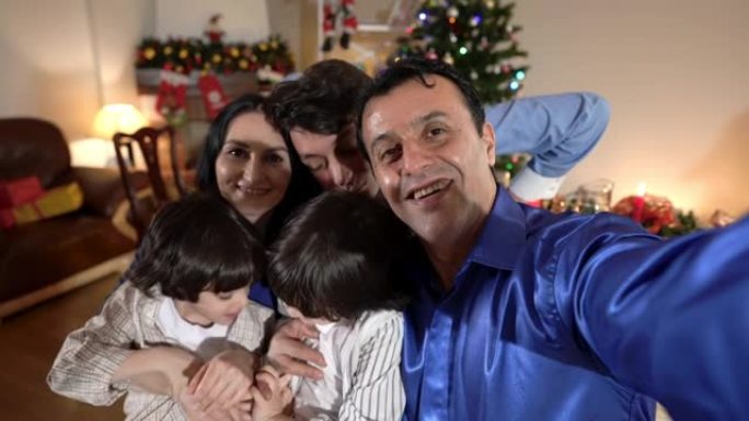 自拍POV快乐中东男子在平安夜在家室内与家人合影。微笑的男人与白人女子少年和双胞胎兄弟一起享受新年庆