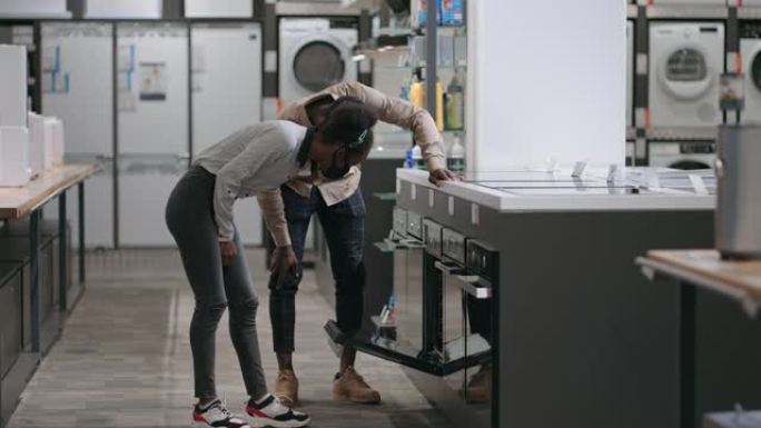年轻的一对正在家用电器商店选择烤箱，美国黑人家庭正在购物，购买厨房设备