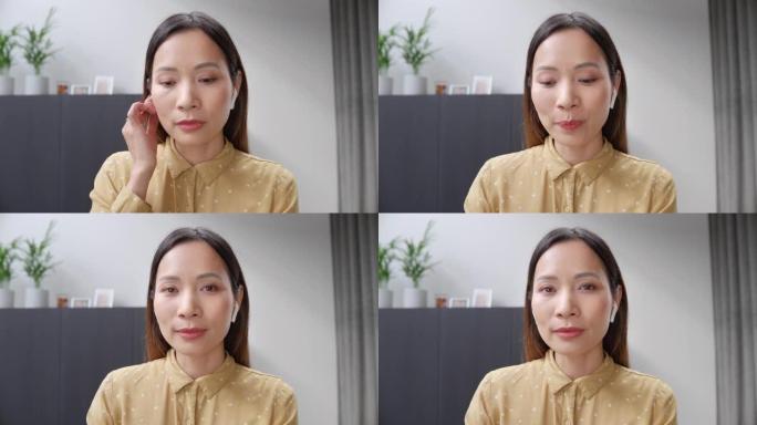 一个亚洲妇女在她的家庭办公室听视频会议电话