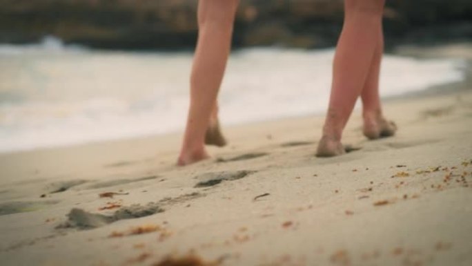 特写两个人的脚走出大海，在海滩后视