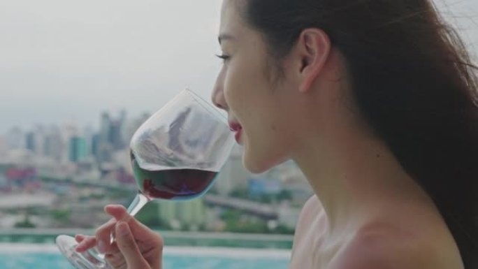 年轻漂亮的女人在豪华度假胜地的游泳池里喝杯红酒。