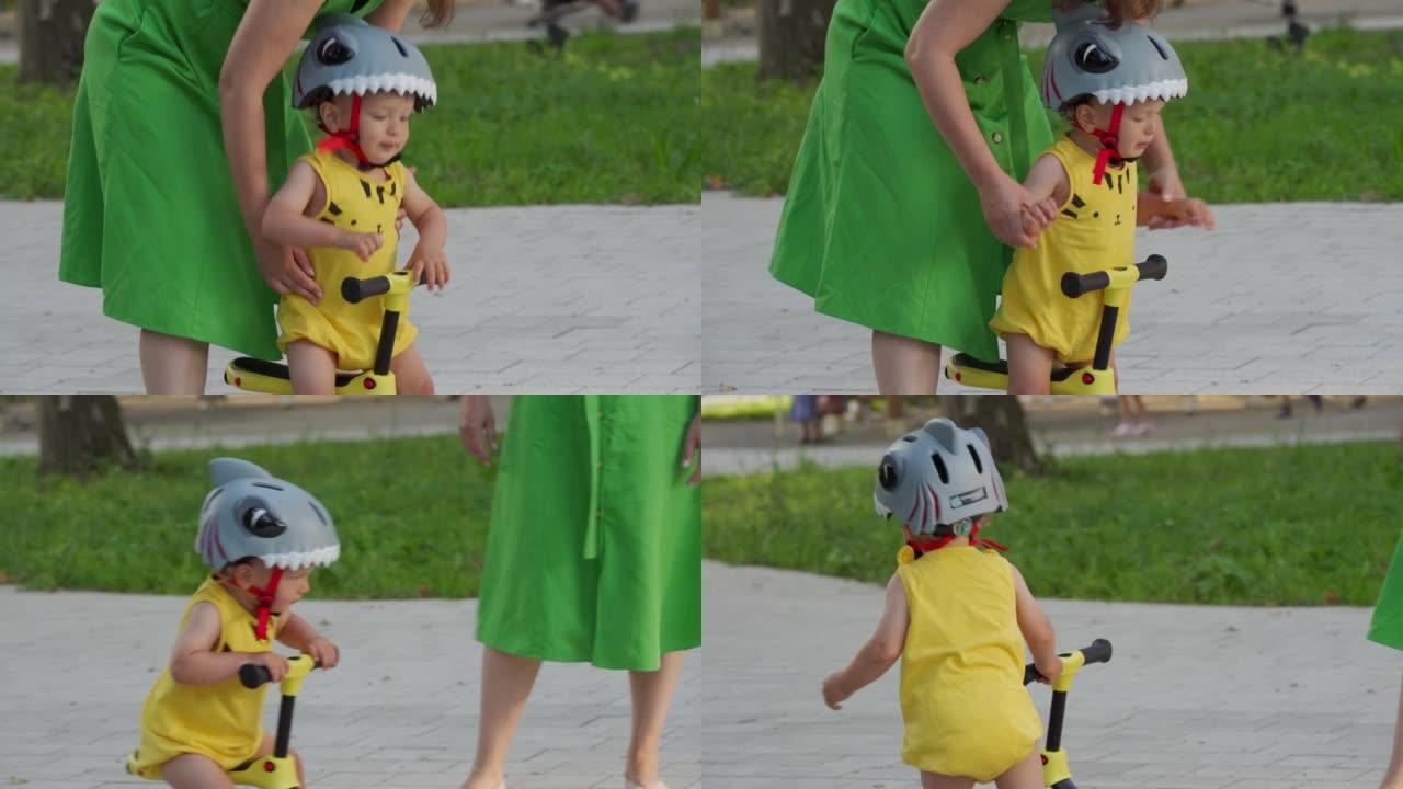 母亲教她的蹒跚学步的孩子在户外骑平衡自行车，1.5岁的孩子和妈妈在夏天在公园里玩脚踢滑板车。