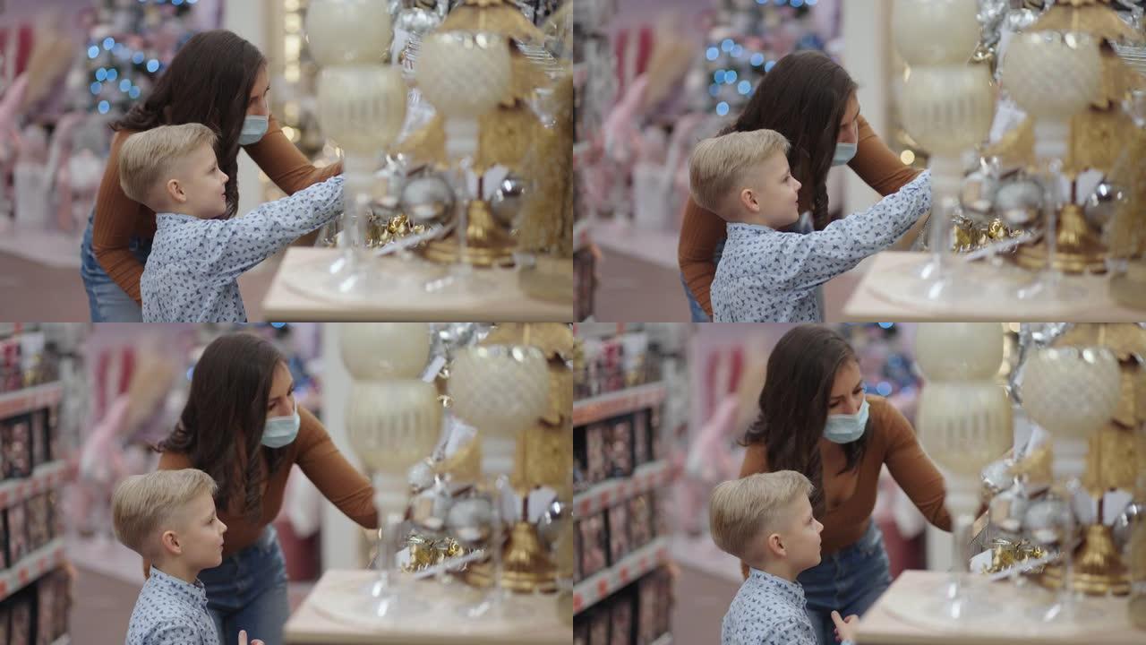 一位戴着医用口罩的母亲和她的儿子在购物中心为圣诞节选择家居装饰品