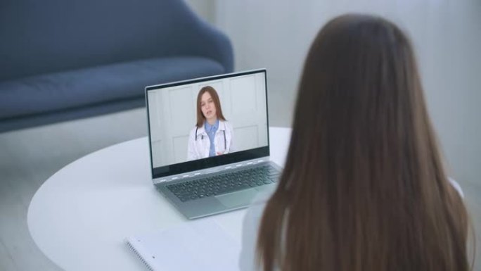 肩部观察年轻女性在第一次病毒疾病症状、医疗保险、covid19传播后，通过笔记本电脑上的视频通话在线