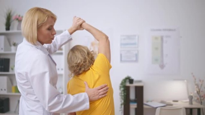 女性创伤专家在诊所帮助高级患者进行伸展运动