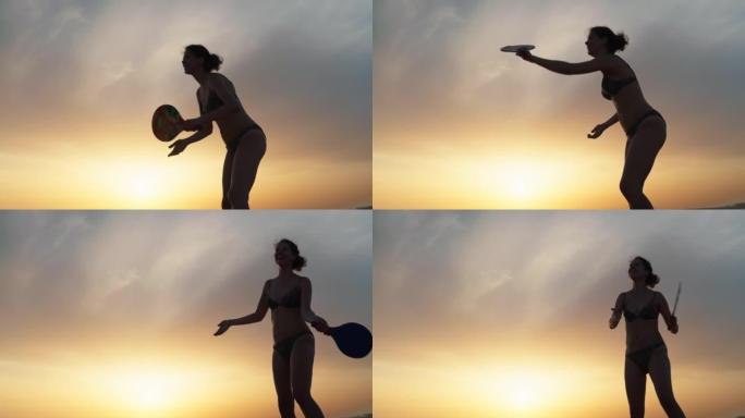 日落时在海滩上享受桨网球的女人的剪影。