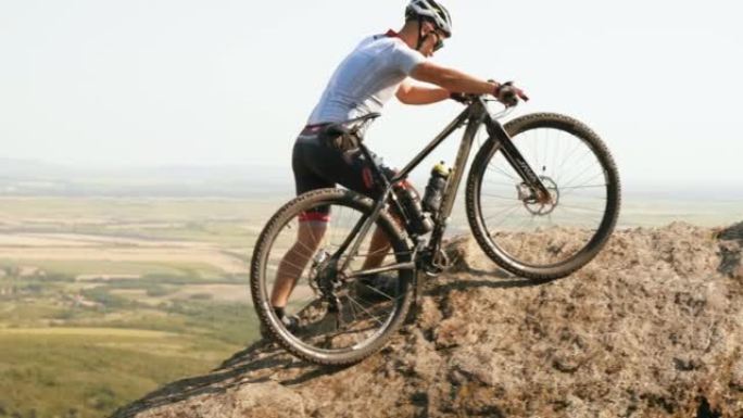 Extreme MTB biker将他的自行车推向岩石顶部