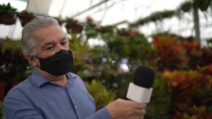 戴口罩的电视记者采访花园商店员工