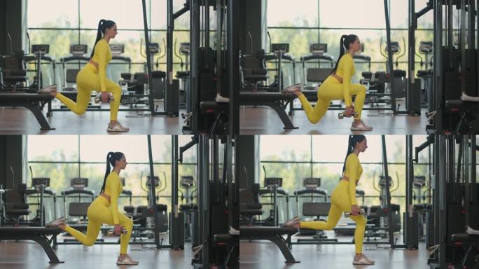 有运动能力的女人在健身房里用哑铃给腿做弓步。年轻肌肉发达的西班牙裔妇女穿着黄色运动服在健身房用哑铃做