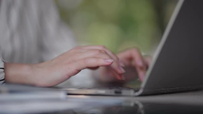 一个女人坐在夏季咖啡馆里在笔记本电脑键盘上打字的特写镜头。自由职业者的远程工作。打印计算机代码