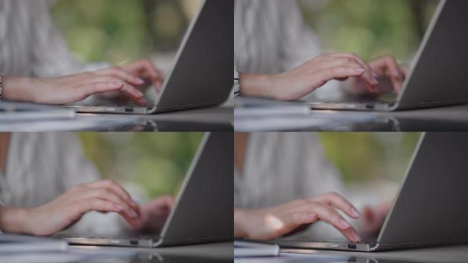 一个女人坐在夏季咖啡馆里在笔记本电脑键盘上打字的特写镜头。自由职业者的远程工作。打印计算机代码