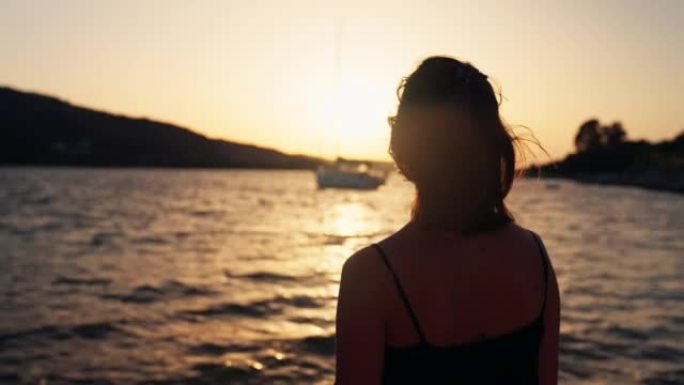 女人在金色的天空下日落时用帆船看海