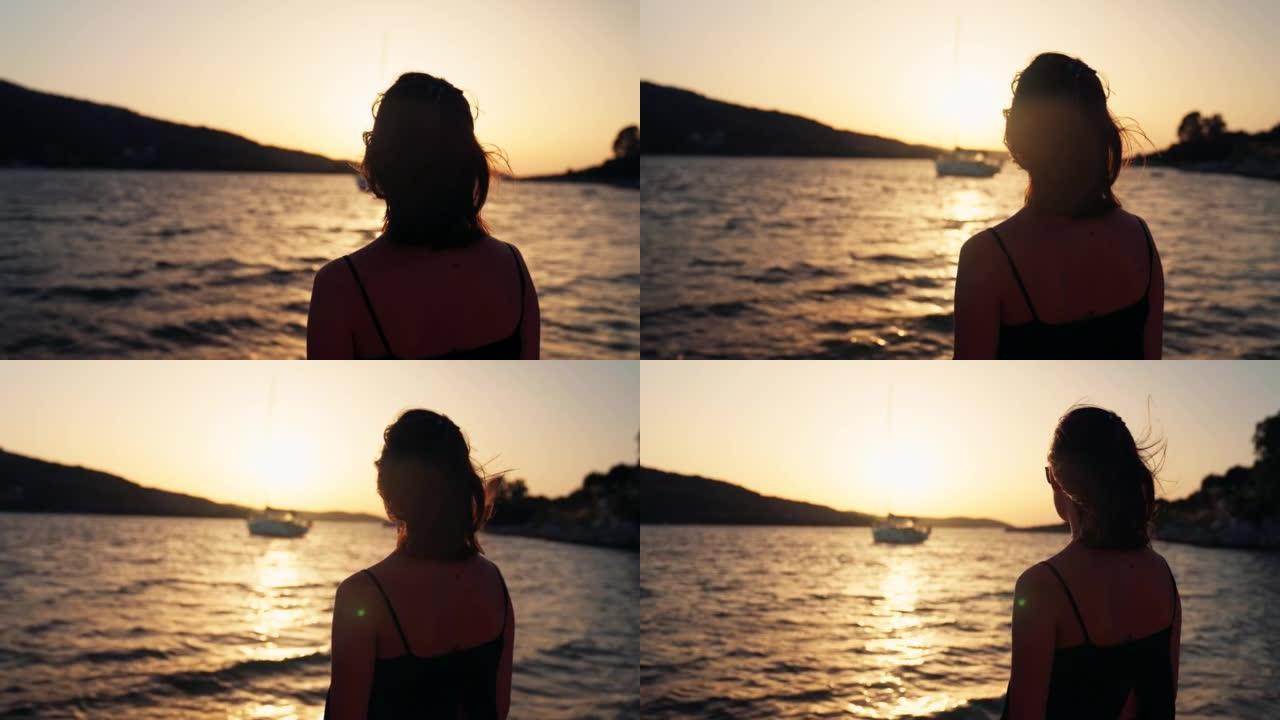 女人在金色的天空下日落时用帆船看海