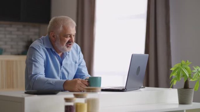 中年男子通过笔记本电脑与朋友或家人进行视频聊天，独自一人坐在家里