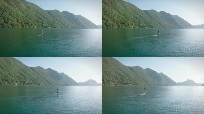 骑电动箔纸在平静的湖上滑行的人包围了我的山脉