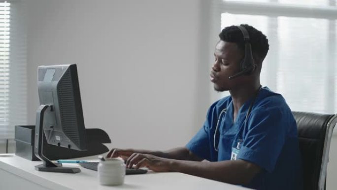 在医院工作的带耳机和计算机的美国黑人男性医生或护士。年轻的专业治疗师医生使用网络摄像头上的远程通信咨