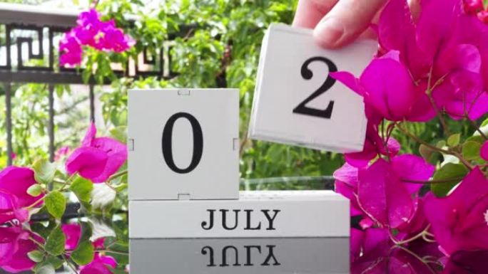 一个木制日历，有一个重要的活动，7月2日在一张有芙蓉花的桌子上，女人的手在日历上设定了日期。将日历翻
