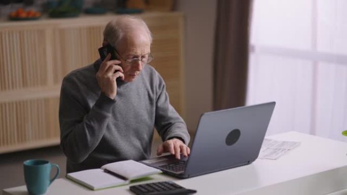 老人在冠状病毒大流行期间在家远程工作，老人正在使用笔记本电脑并通过电话打电话