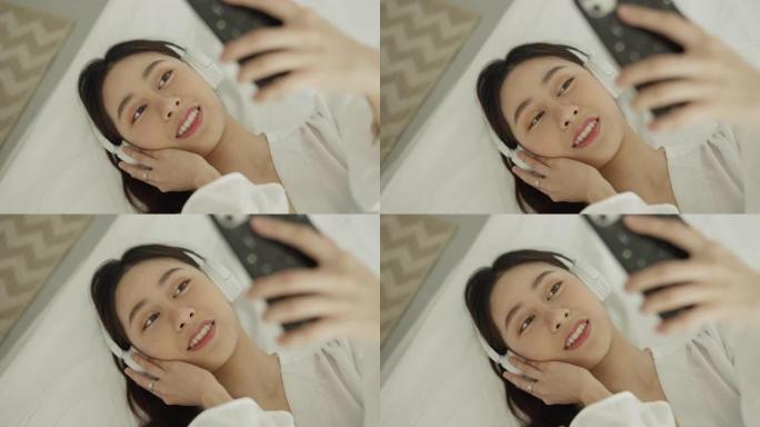 女人在床上使用带耳机的智能手机