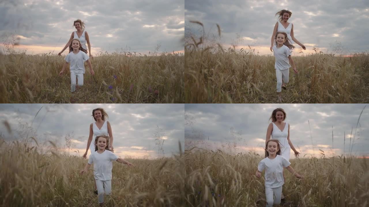 女儿和母亲的梦想在日落时一起在麦田里奔跑。麦田概念中的幸福家庭人。妈妈和女孩玩追赶跑。在绿色草地上奔