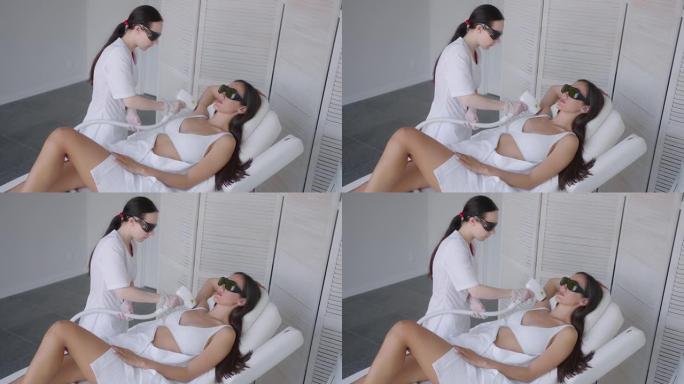 美容师做腋下激光脱毛迷人性感女人躺在医疗沙发上，在美容院微笑。美容师做激光脱毛病人的腋窝。脱毛程序