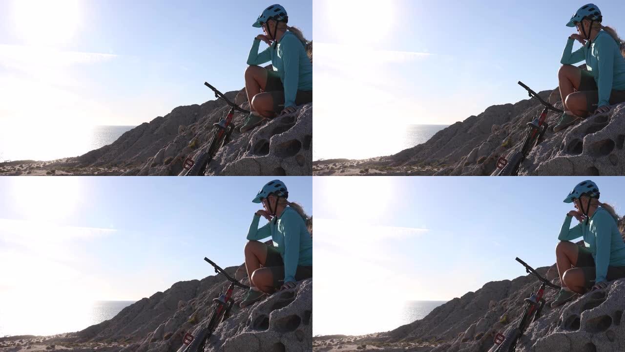 女性山地自行车手在海上的岩石山脊上放松