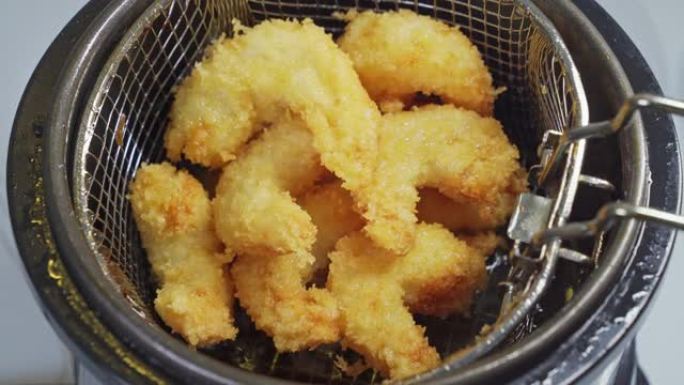 从油炸锅里拿出一个篮子，里面装着面糊的炸虾。