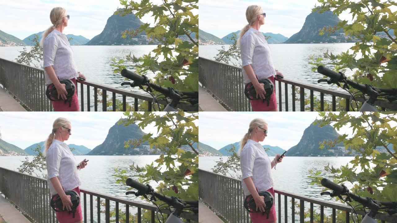 女人使用智能手机在俯瞰湖泊的栏杆上放松