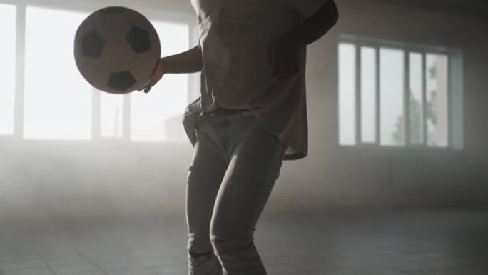 一个特写的黑人在车库的阳光下玩足球。城市环境中日落时的足球自由泳。灰尘和日落