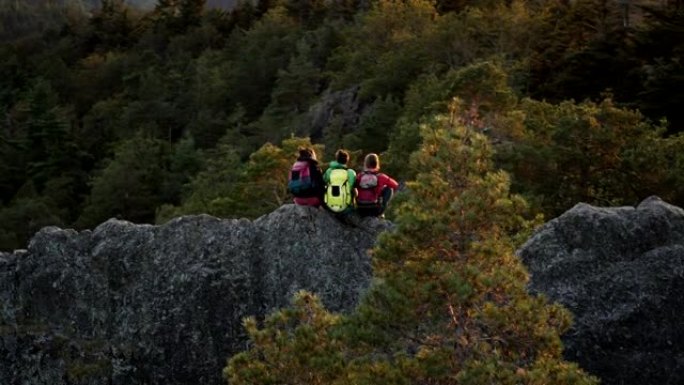 空中无人机拍摄的三名山地自行车手坐在日落时休息的岩石山脊上