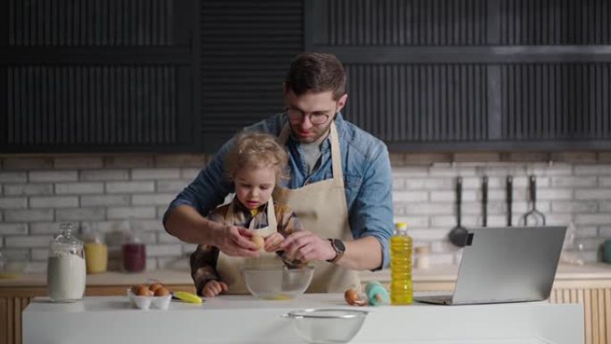 爸爸和小儿子在厨房共度时光，孩子正在学习做饭，在碗里打碎鸡蛋