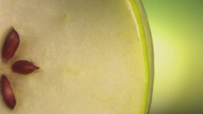 一滴绿色果汁从成熟多汁的绿色苹果片的表面流下。慢动作4K