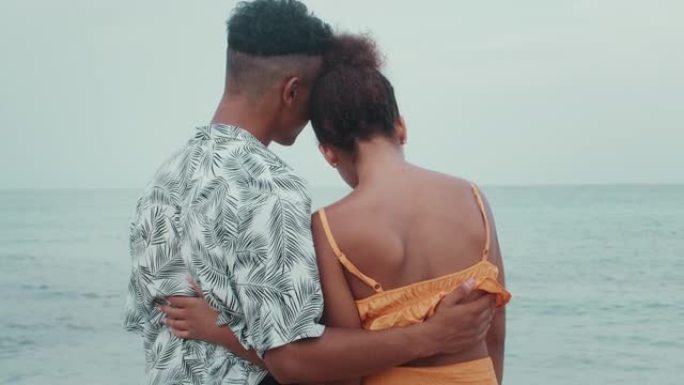热爱非洲种族的夫妇在海滩上拥抱。远望大海
