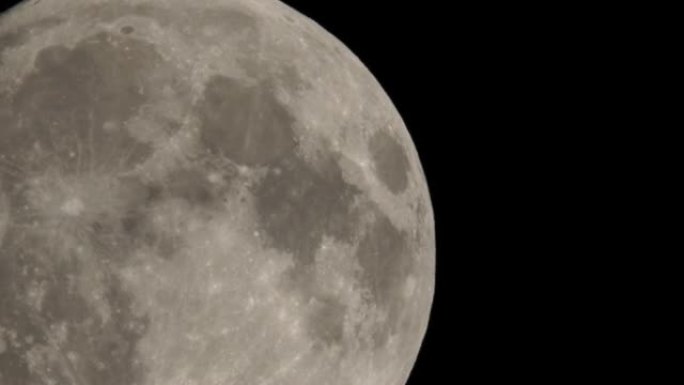 满月在深黑色的天空背景下，用很长的远摄镜头从地球表面拍摄。灰白色的月亮在晴朗的天空中发光。