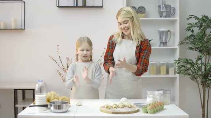 微笑的金发妈妈和女儿一起烘烤，从手中甩掉面粉