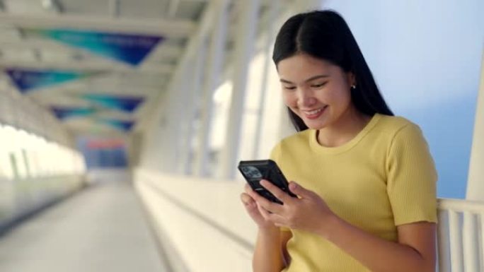 亚洲女子在玩手机的路上连接车站在线购物和社交媒体。