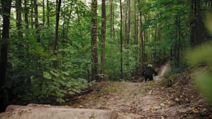 戏剧性的山地自行车空气在森林小径上跳过相机。一个戴着头盔的男子在山地自行车道上高速跳过森林跳板的电影