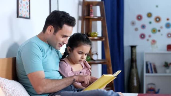 一位年轻的印度父亲和他的小女儿正在读书-夜间故事，就寝时间，过去最喜欢的时间，孩子的教育
