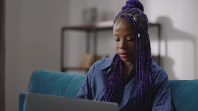 美国黑人女性seo专家正在远程工作，在家中使用笔记本电脑，坐在房间的沙发上，肖像