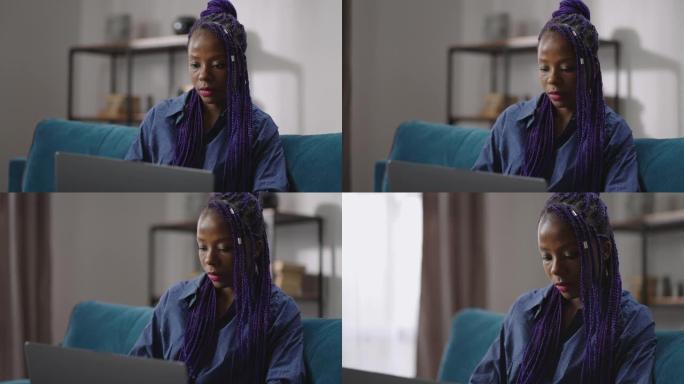 美国黑人女性seo专家正在远程工作，在家中使用笔记本电脑，坐在房间的沙发上，肖像