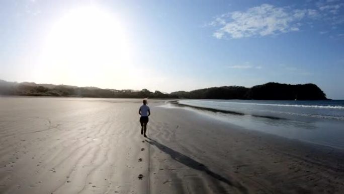 年轻女子在日出时沿着空旷的海滩奔跑