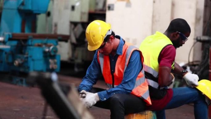 又累又热。亚洲男性和非裔美国工程师工人戴着安全安全帽头盔。金属车床工业制造厂