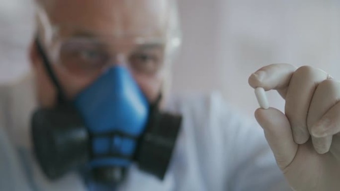 一家制药公司的科学家一名戴着蓝色呼吸器和安全眼镜的药品开发商拿着一种新药一颗白色药丸看着它